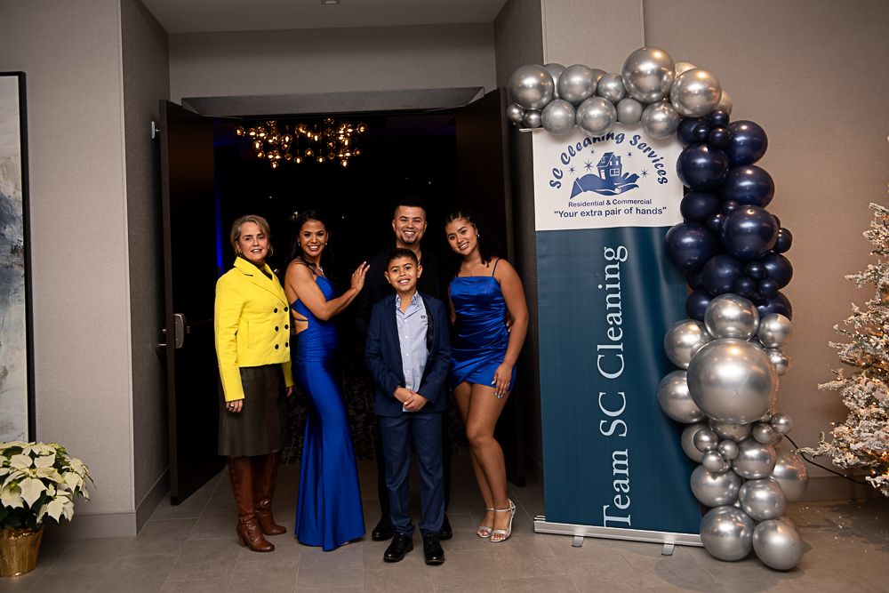 Family posing by a banner with balloons. They are in formal attire, smiling, in front of a doorway.