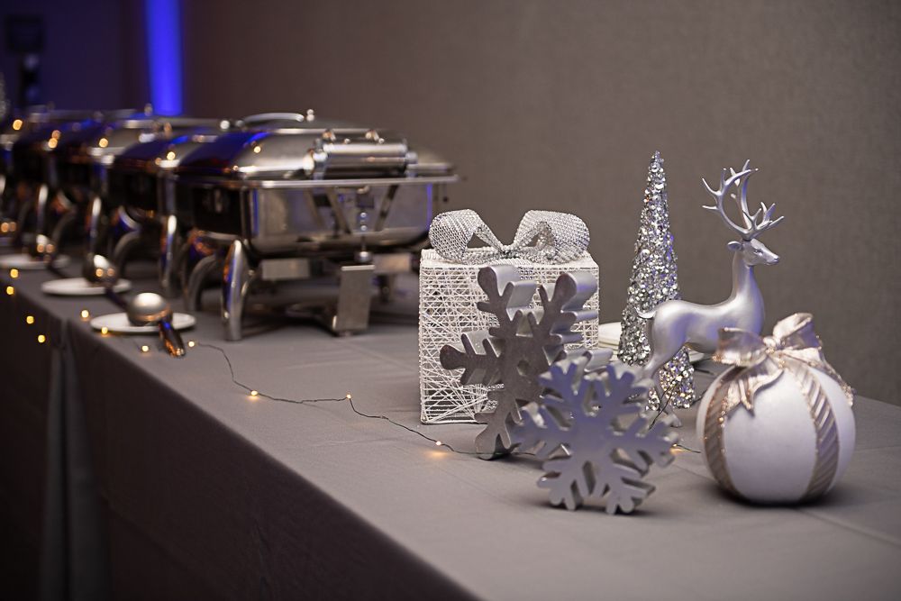 Buffet with silver chafing dishes and holiday decorations on a gray table.