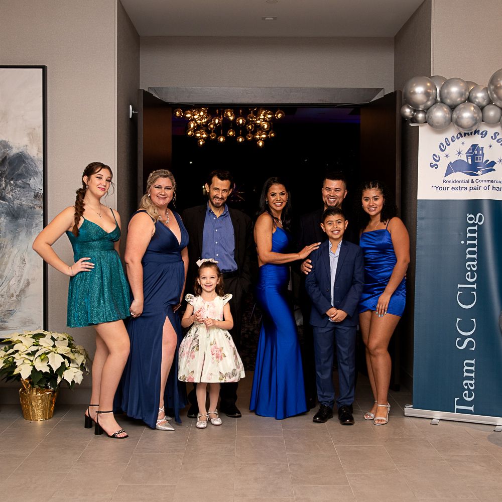 Group poses at an event: People in formal wear in an entranceway with a banner for