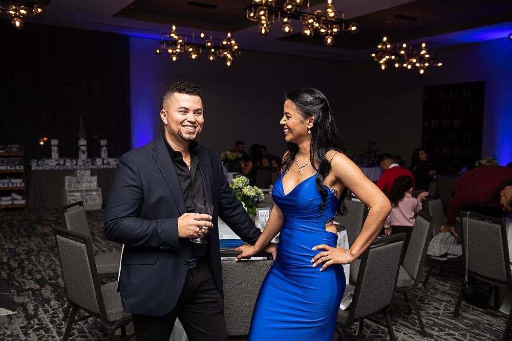 Man and woman smiling at each other in a formal event setting. Man in blazer, woman in blue gown.