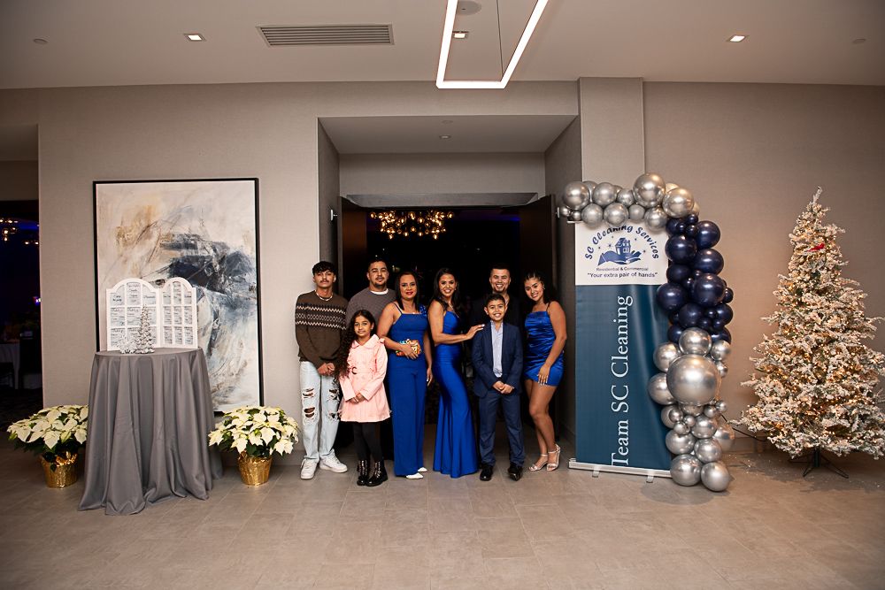 Group of people at an event pose by a balloon arch and Christmas tree.