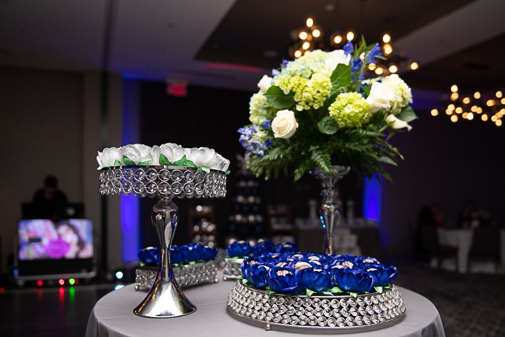 Table display with floral arrangements and silver cake stands in a dimly lit event space.