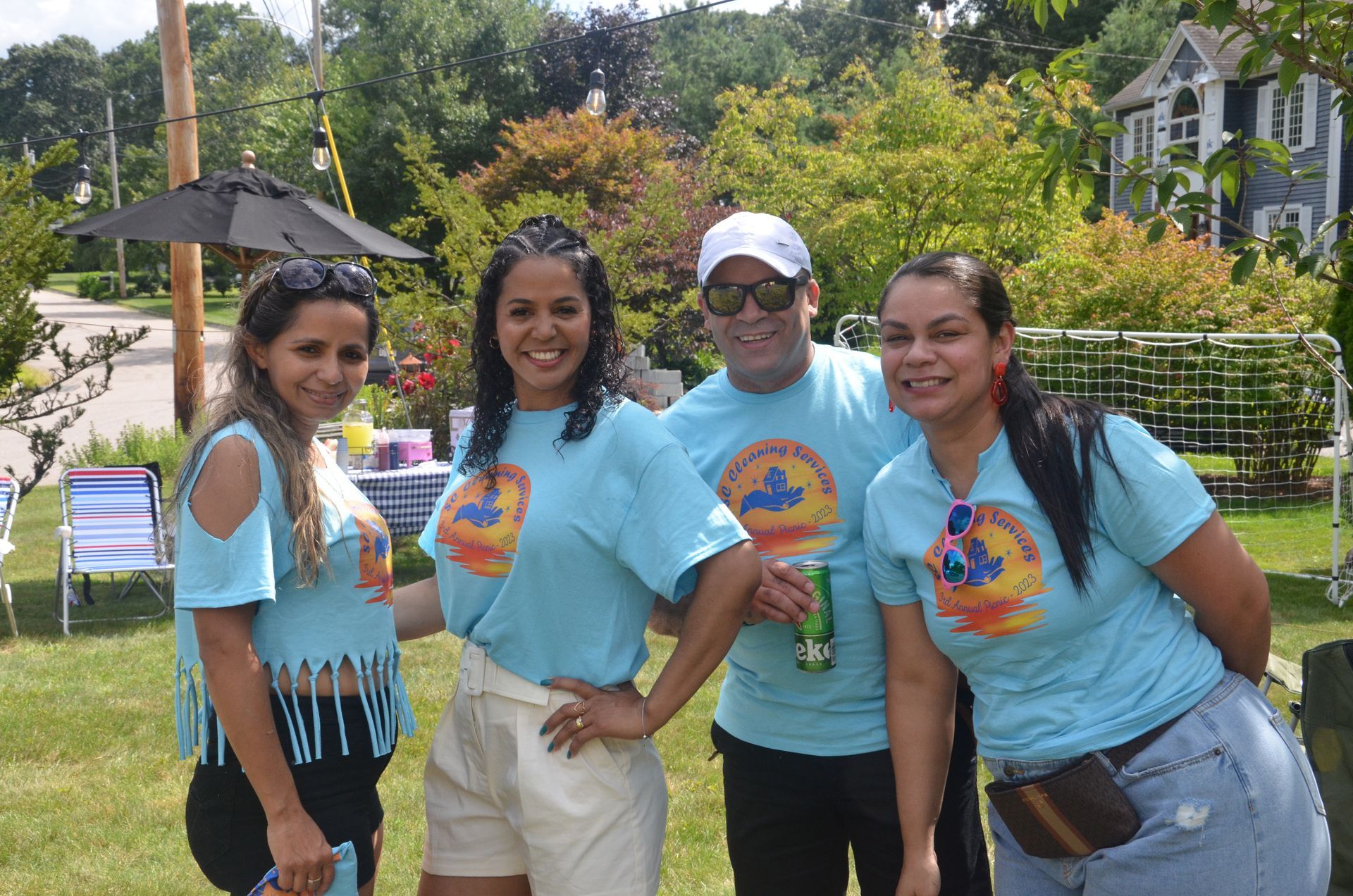 Four people smiling outdoors, wearing matching blue t-shirts with logo.