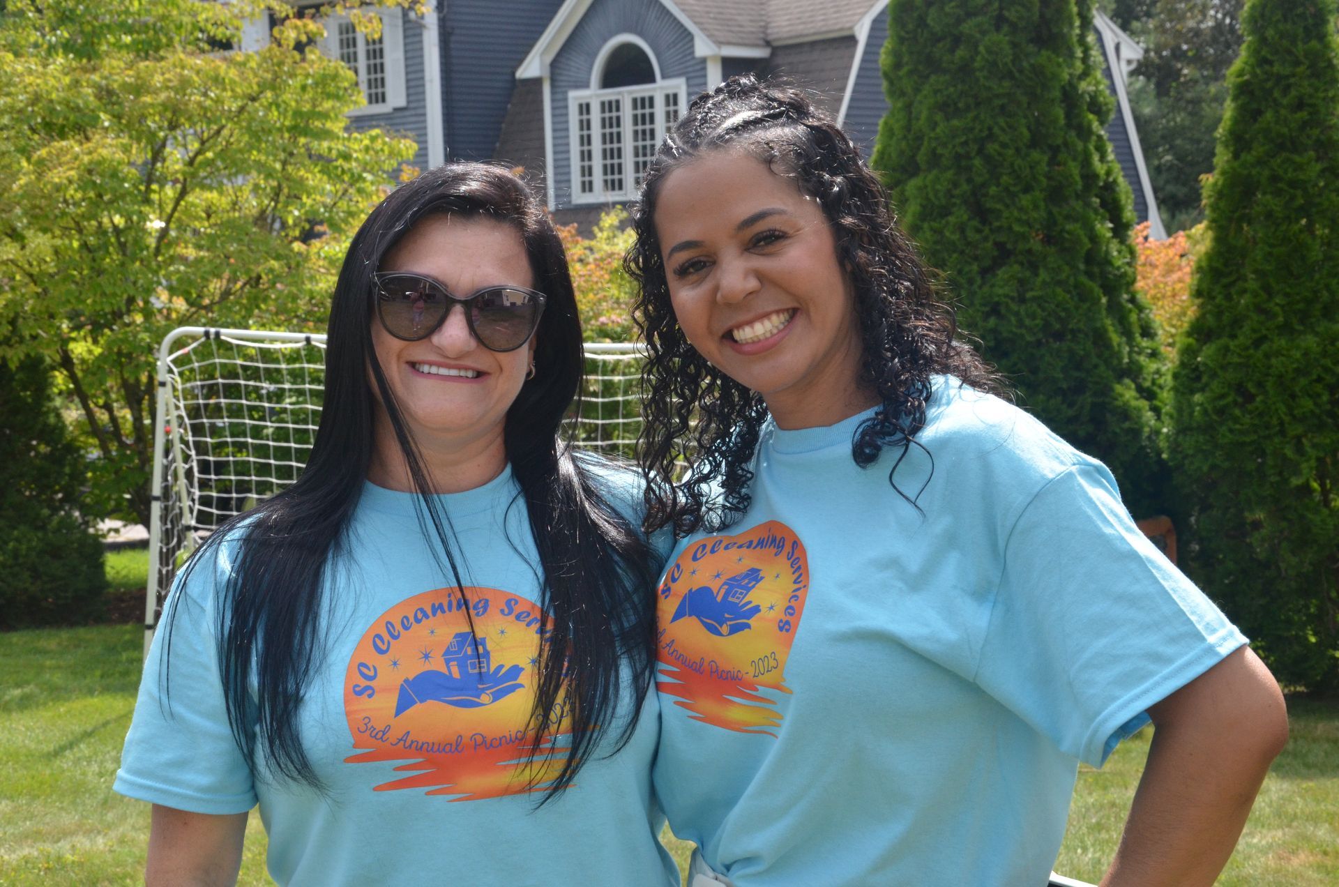 Two women in blue shirts smile outdoors.