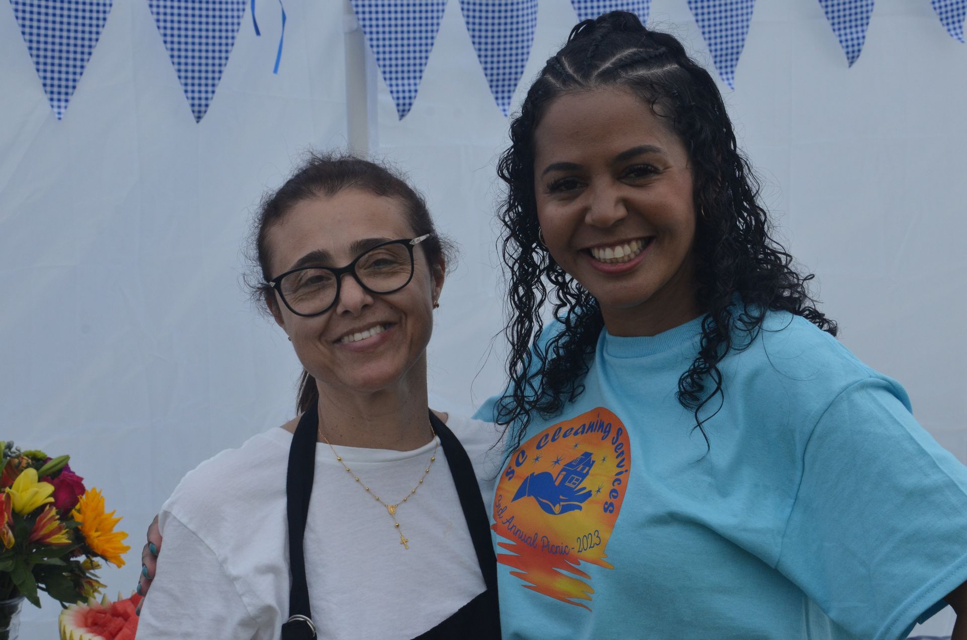 Two smiling women pose for a photo outdoors with a festive backdrop.