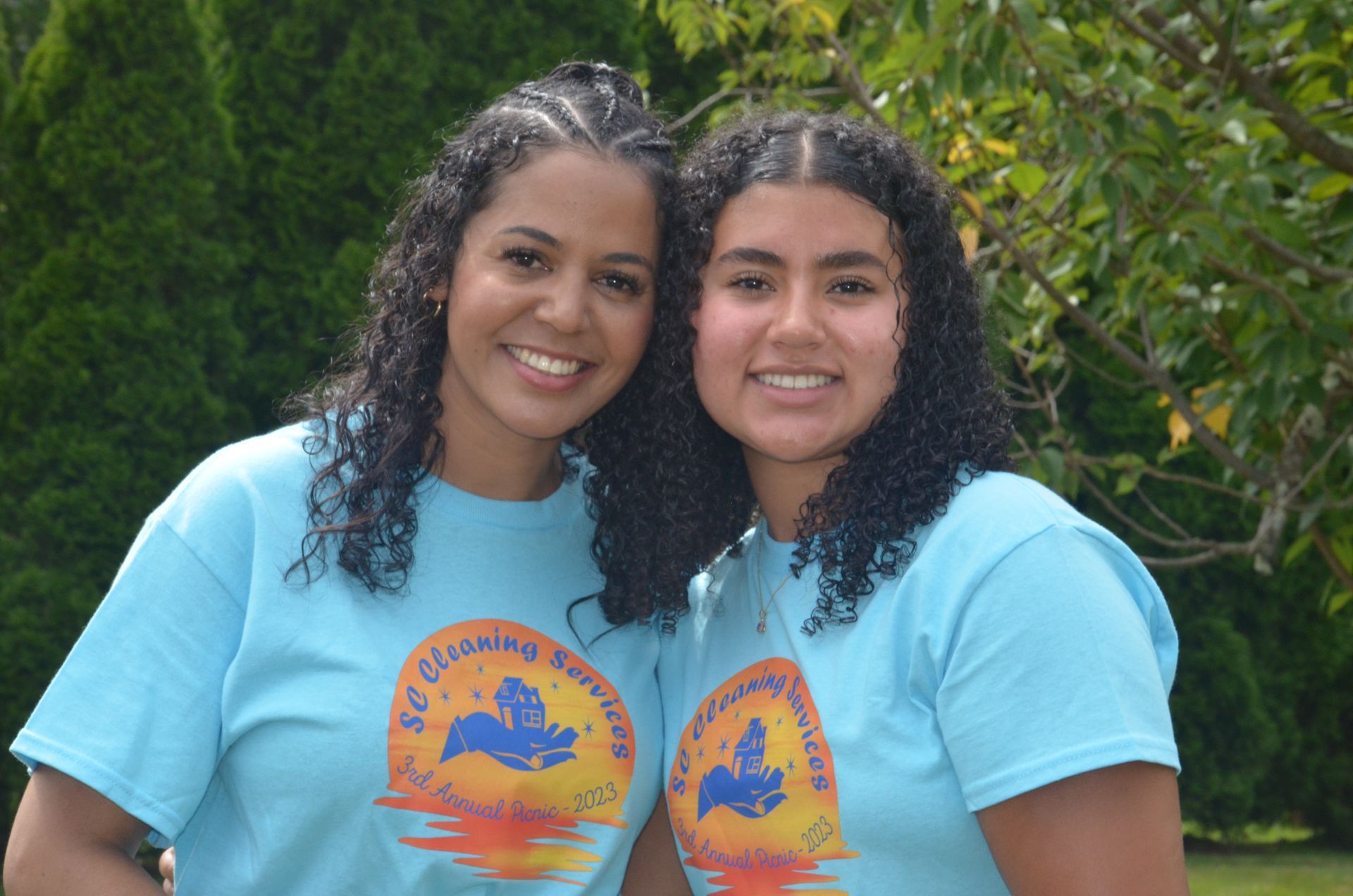 Two women, smiling, wearing matching blue t-shirts outdoors.