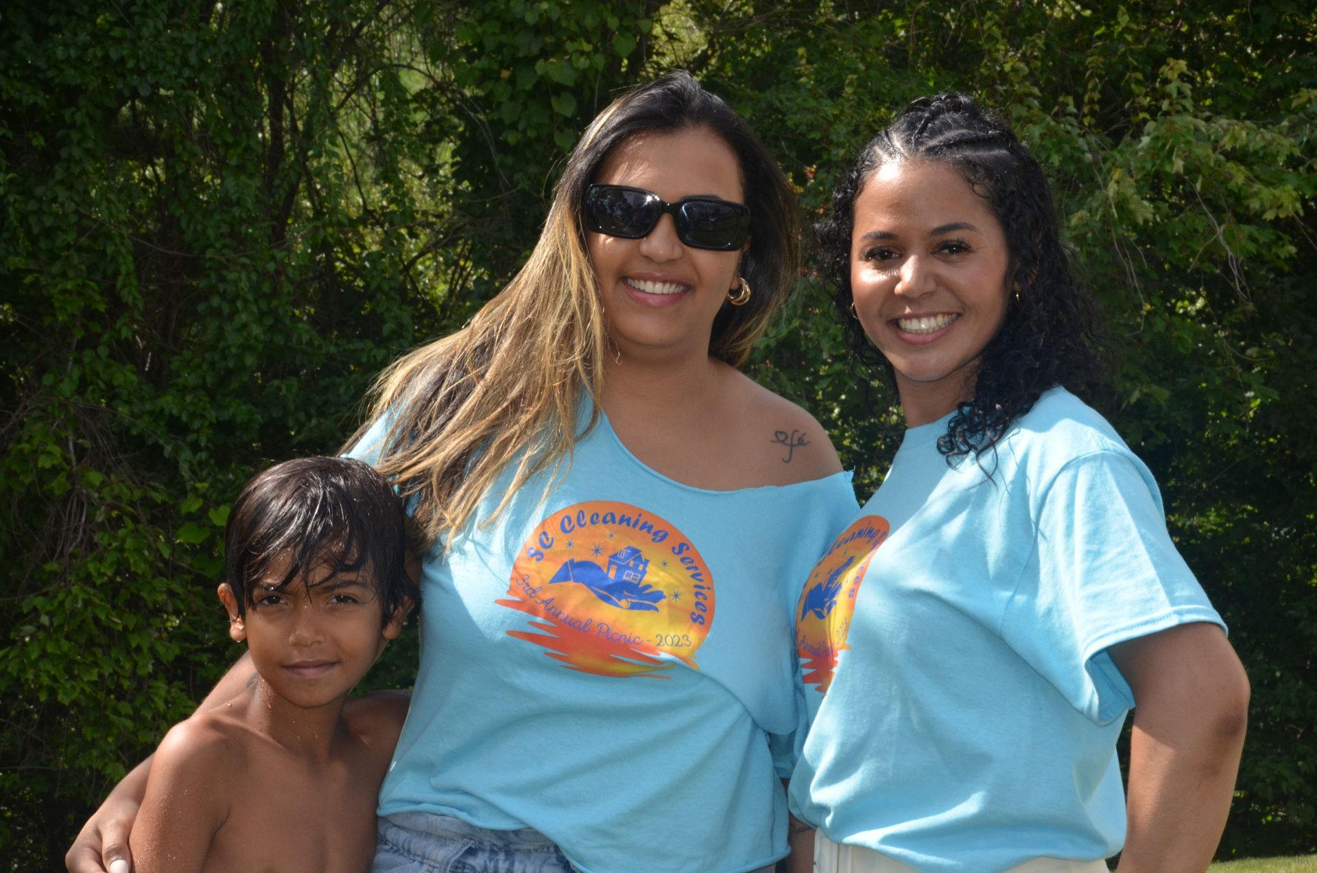 Two women and a boy wearing matching light blue shirts in a backyard.