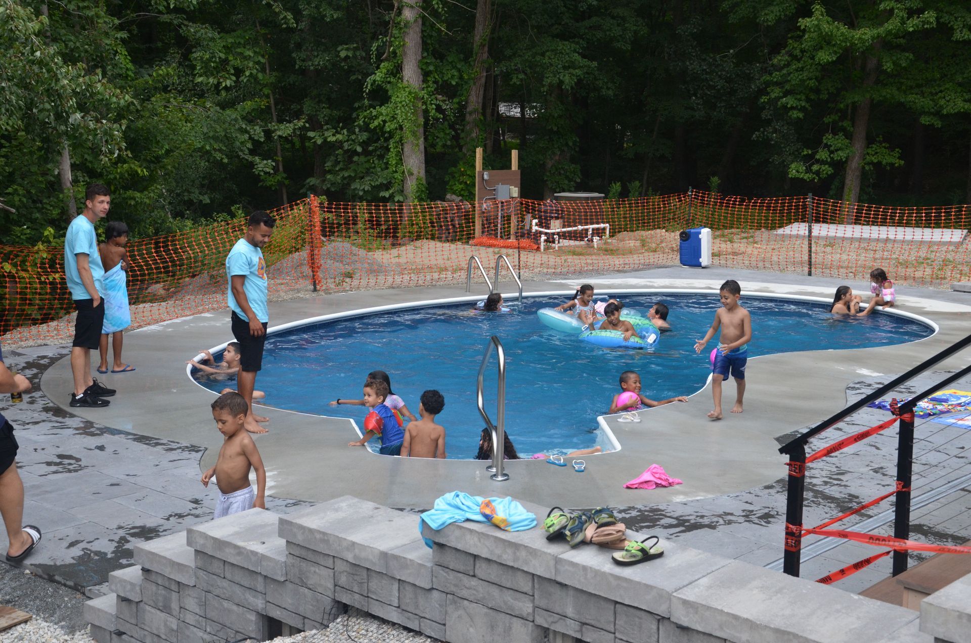 Children and adults in a swimming pool. Some playing, others supervised. Concrete steps and a deck are in view.