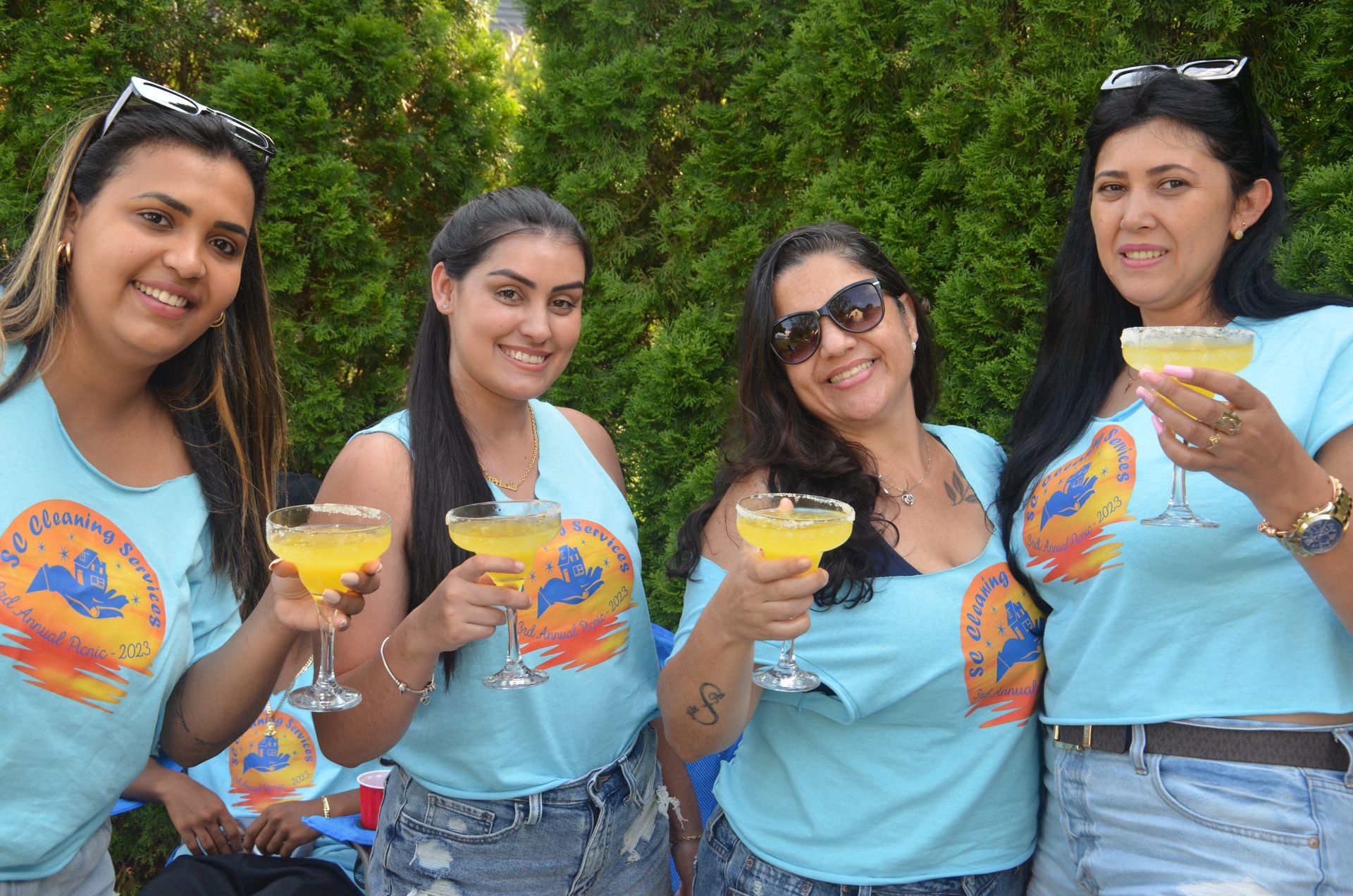 Four women in blue shirts holding cocktails, smiling, standing outside.