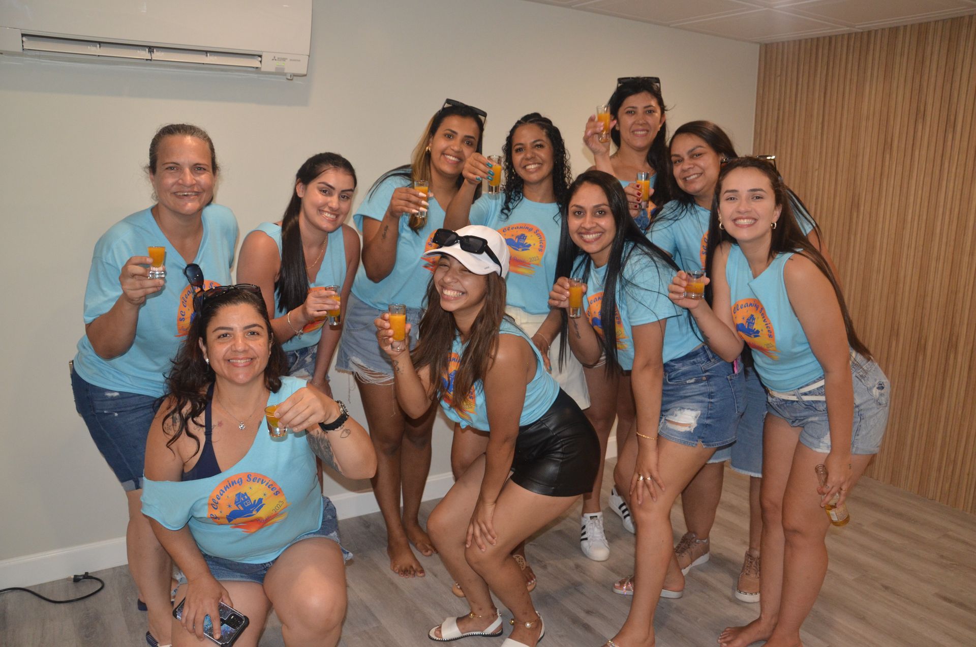 Group of women in blue shirts and shorts celebrating with drinks. Indoors.