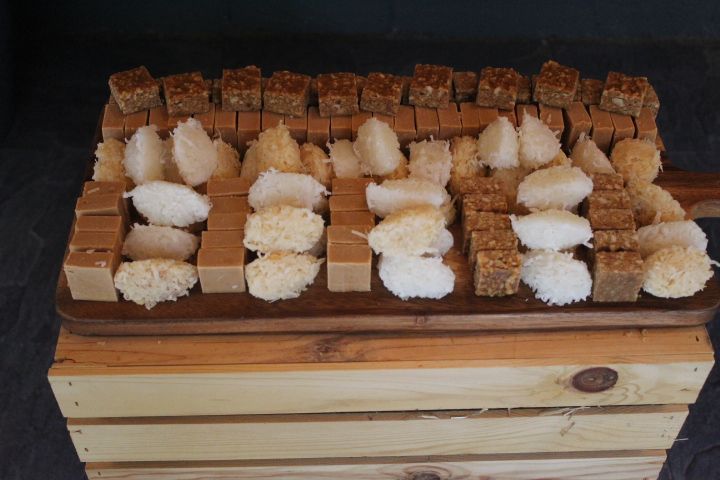 Wooden tray with various Brazilian candies: coconut, peanut, and caramel squares, atop a wooden crate.