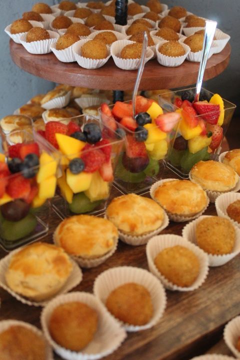 Catering display with savory pastries, fruit salad cups, and mini fried snacks arranged on tiered platters.