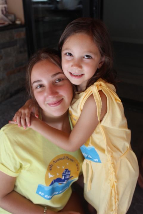 Two smiling girls hugging, wearing matching yellow shirts.