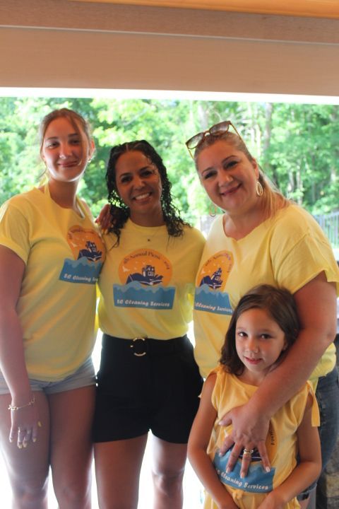 Four people, two adults and two children, smiling in yellow shirts. Outdoor setting.