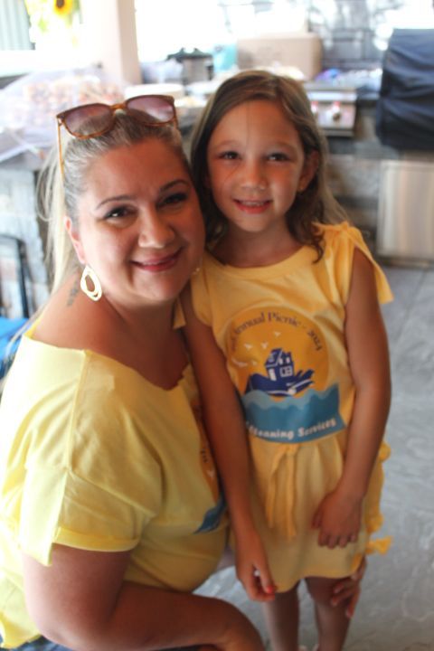 Woman and young girl in yellow shirts smiling, posing outdoors.