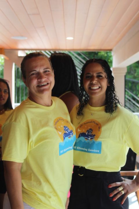 Two smiling women in yellow shirts posing outdoors.
