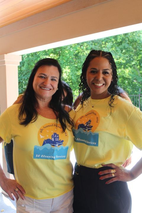 Two women wearing yellow shirts, smiling, posing outdoors.
