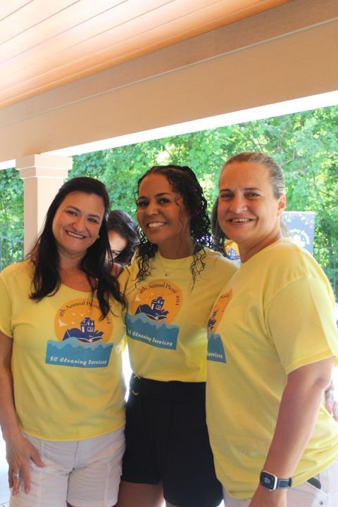 Three women in yellow shirts pose together, smiling outside.