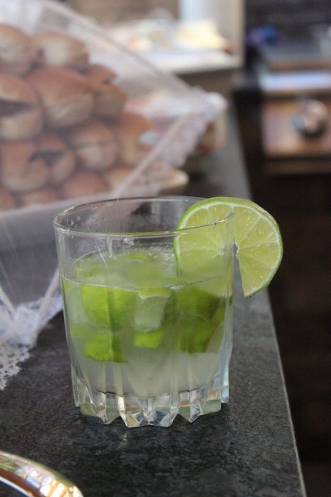 Glass of Caipirinha cocktail with lime slice on a black surface.