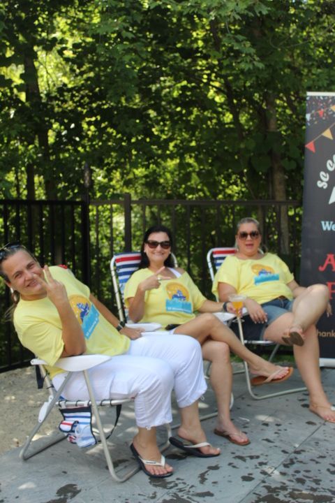 Three people in yellow shirts sit in folding chairs outdoors, smiling.