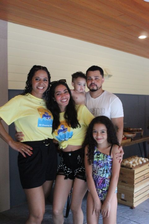 Family posing together indoors; people smiling; child in swimsuit.