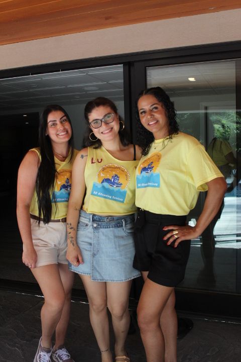 Three women in yellow shirts, posing outdoors. One wears jean skirt, others shorts. Smiling.