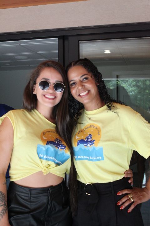Two women smiling, wearing matching yellow t-shirts, standing near a glass door.