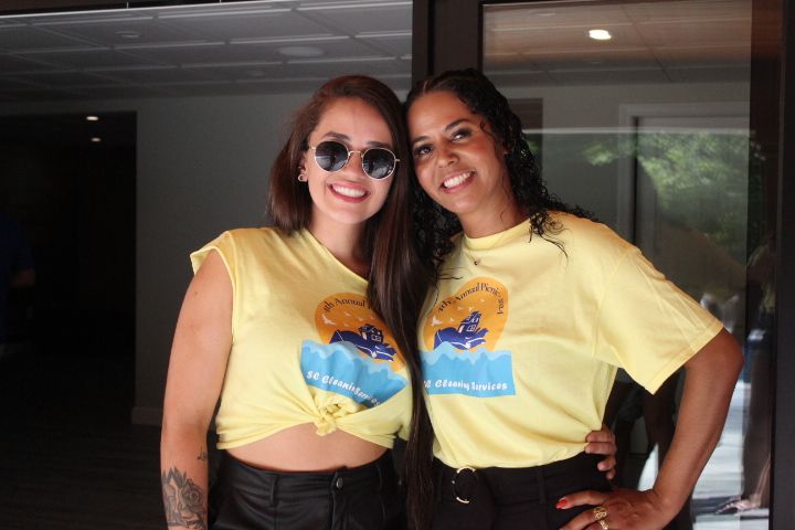 Two women in yellow shirts, posing together. They are smiling. The shirts have a logo.