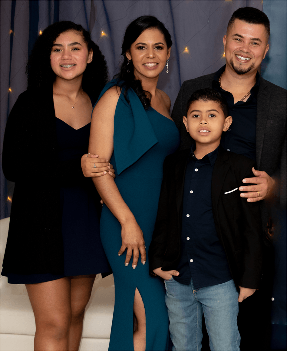 Family of four, posing. Woman in teal dress, man in blazer, boy and girl. Cheerful expressions.