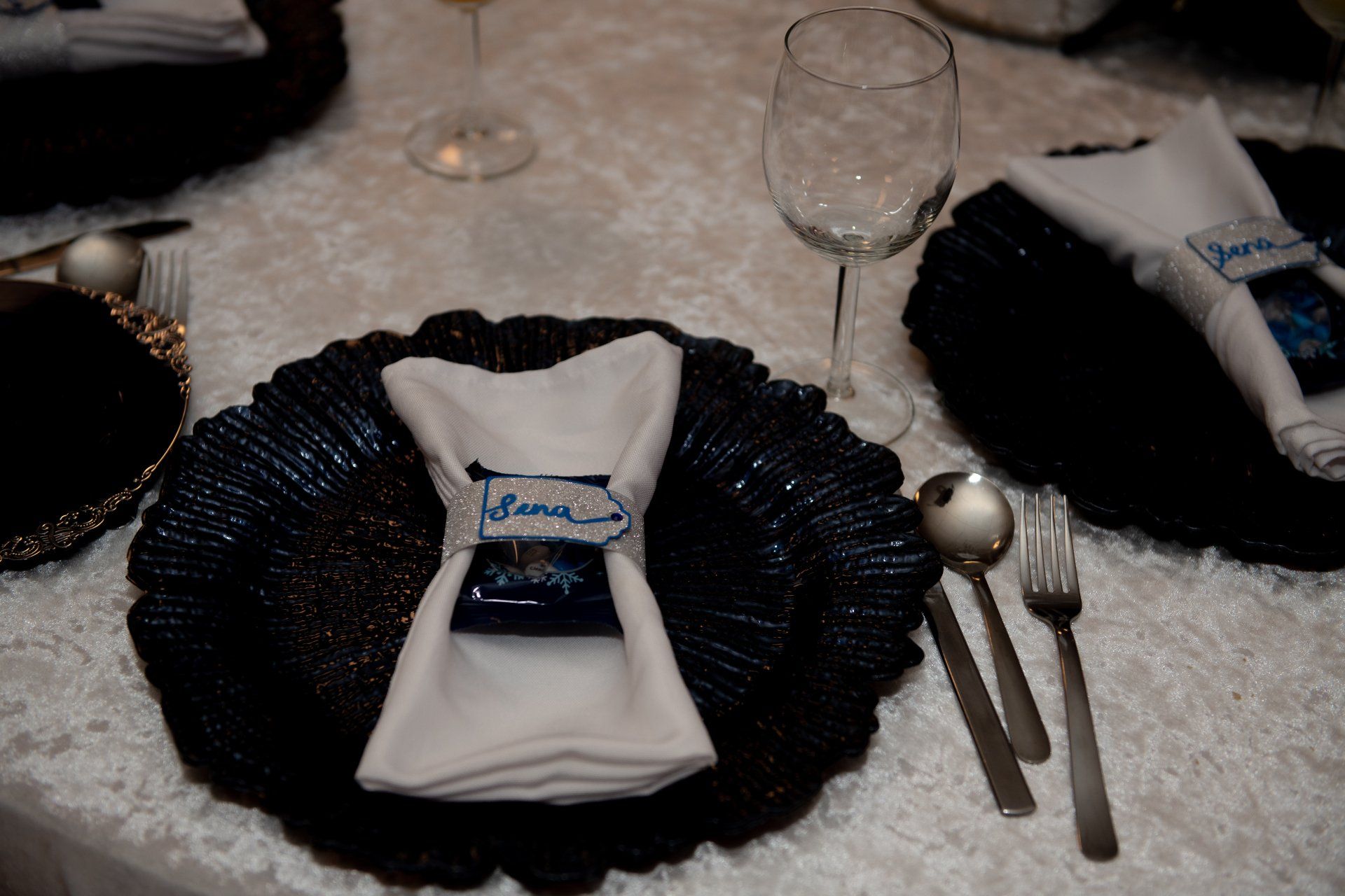 Elegant table setting with navy charger plate, white napkin, name card, silverware, and wine glass.
