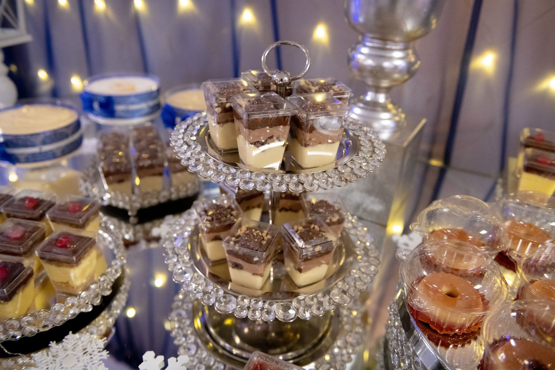 Dessert table with tiered trays of mini cakes and pastries. White and silver decor.