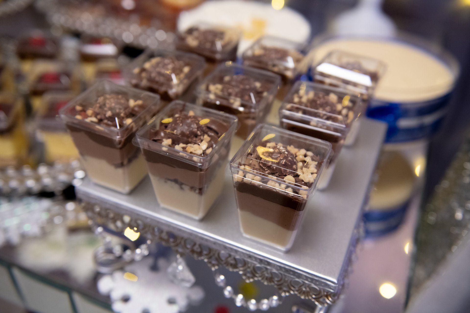 Dessert cups with layers of cream, chocolate, and nuts, on a silver serving tray.