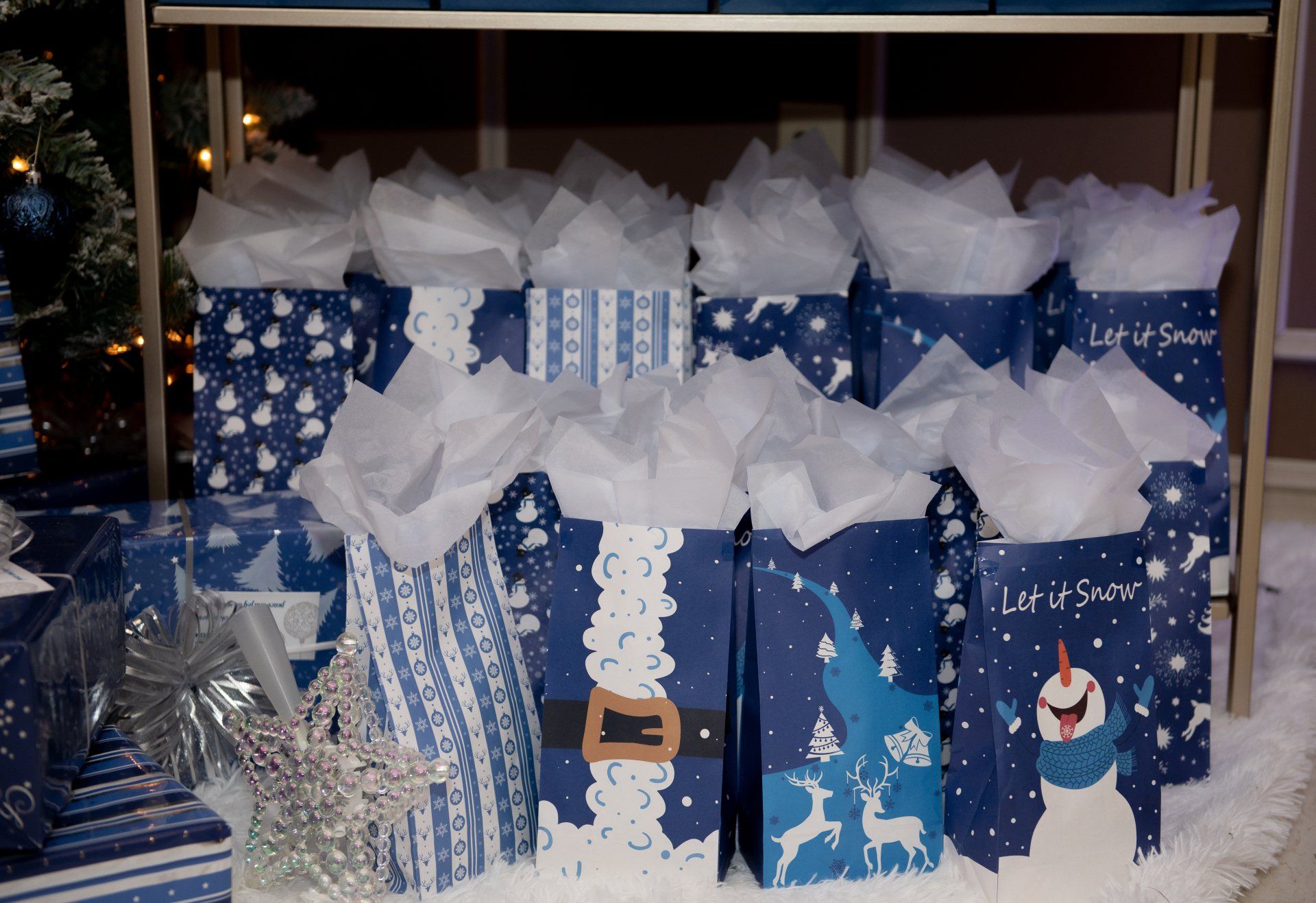 Blue gift bags with tissue paper, featuring wintery designs, stacked on a shelf.