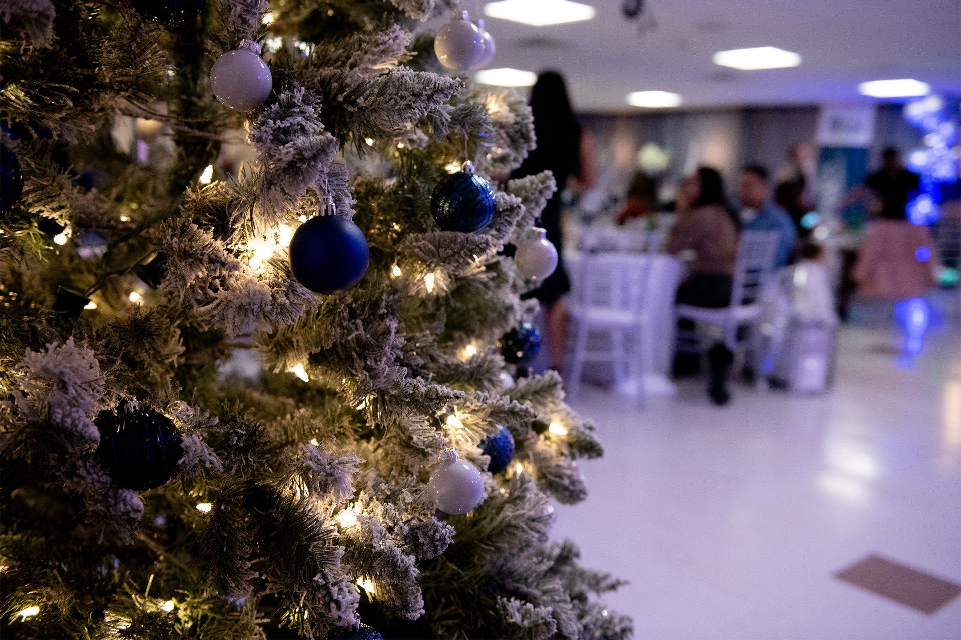 Christmas tree with blue and white ornaments, in front of a blurry event.