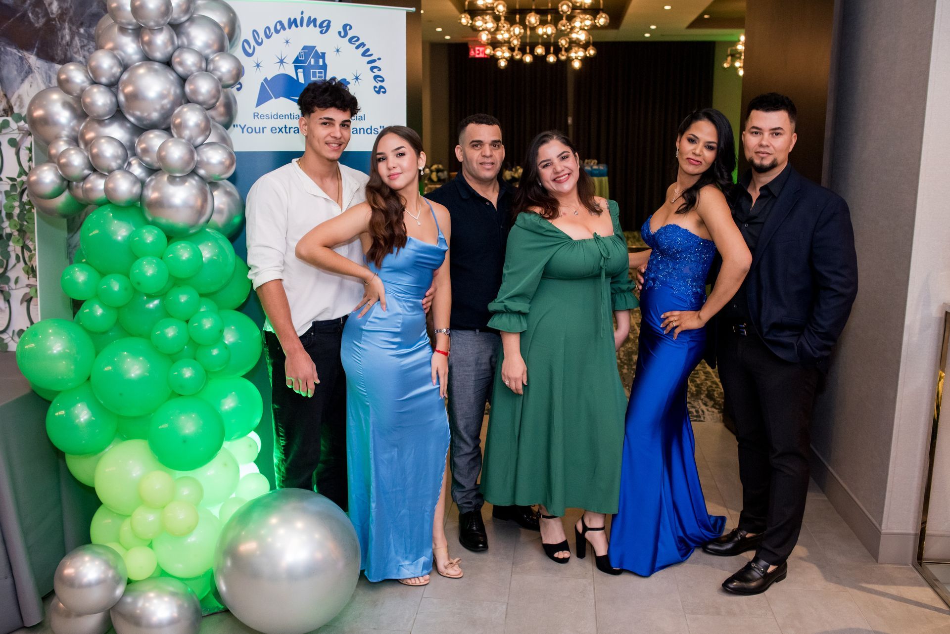 Group of six people posing by balloons, wearing formal attire. Indoors.