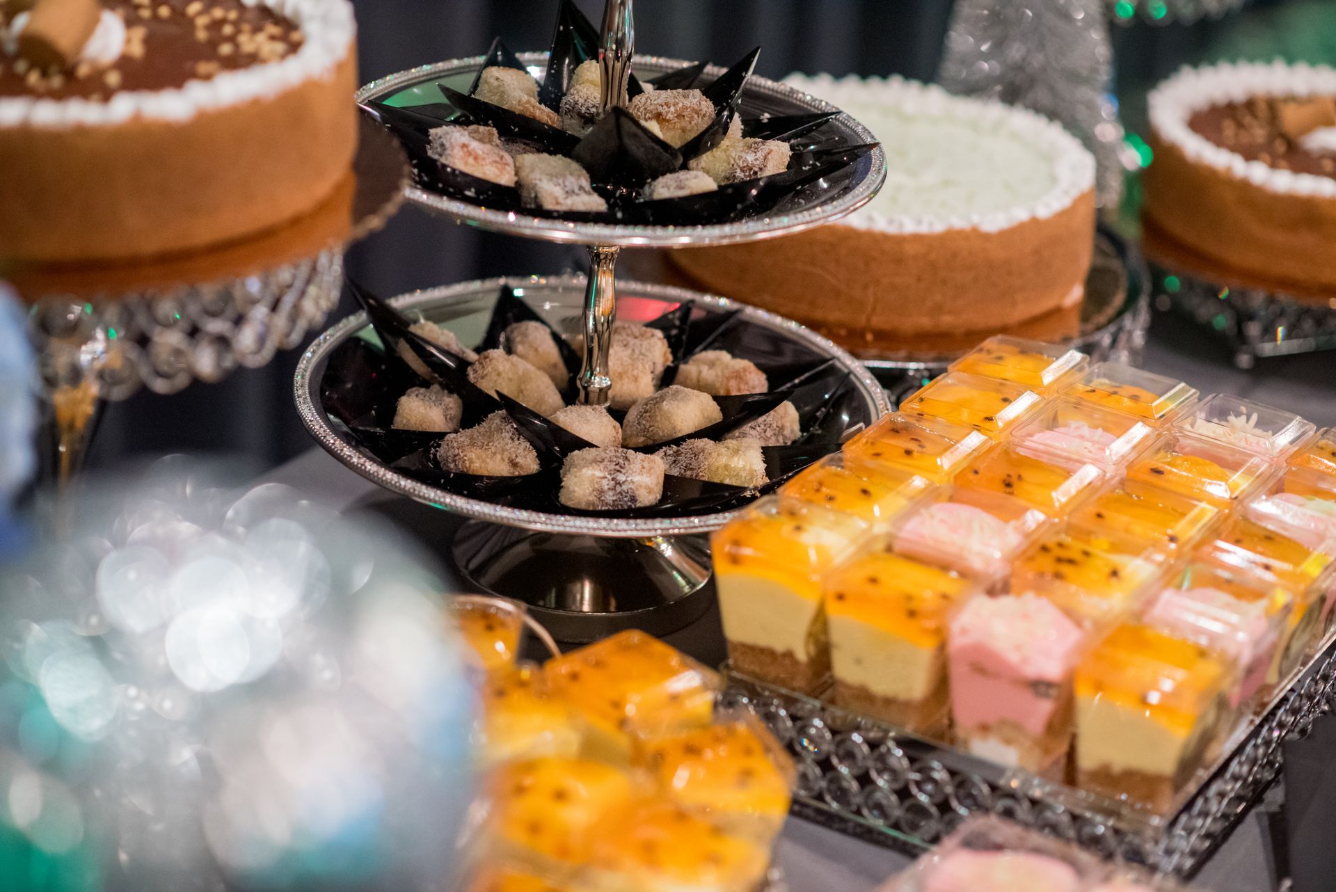 Dessert table with cakes, pastries, and tiered serving trays filled with sweets, silver and white decor.