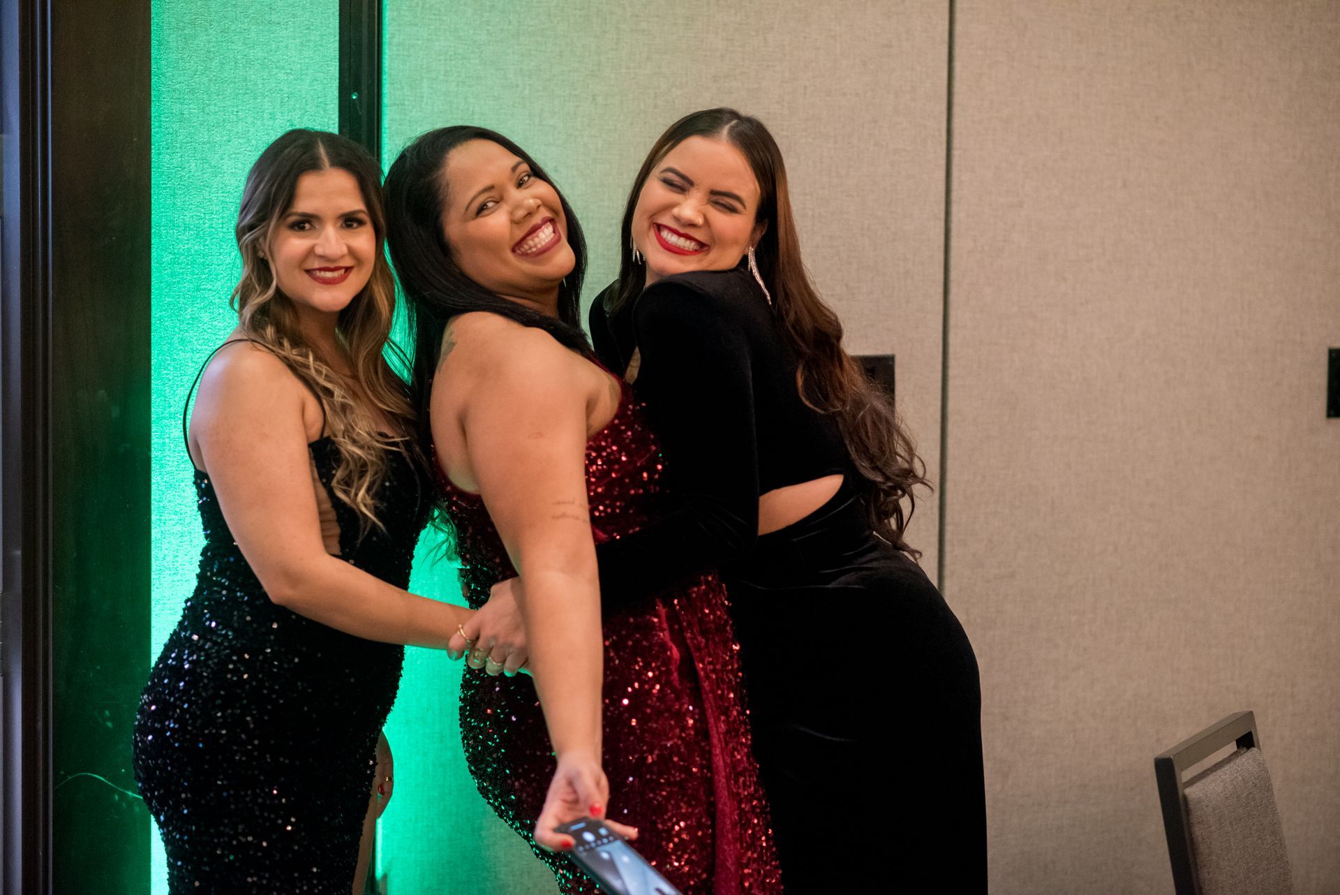 Three smiling women in formal wear pose together at an event.