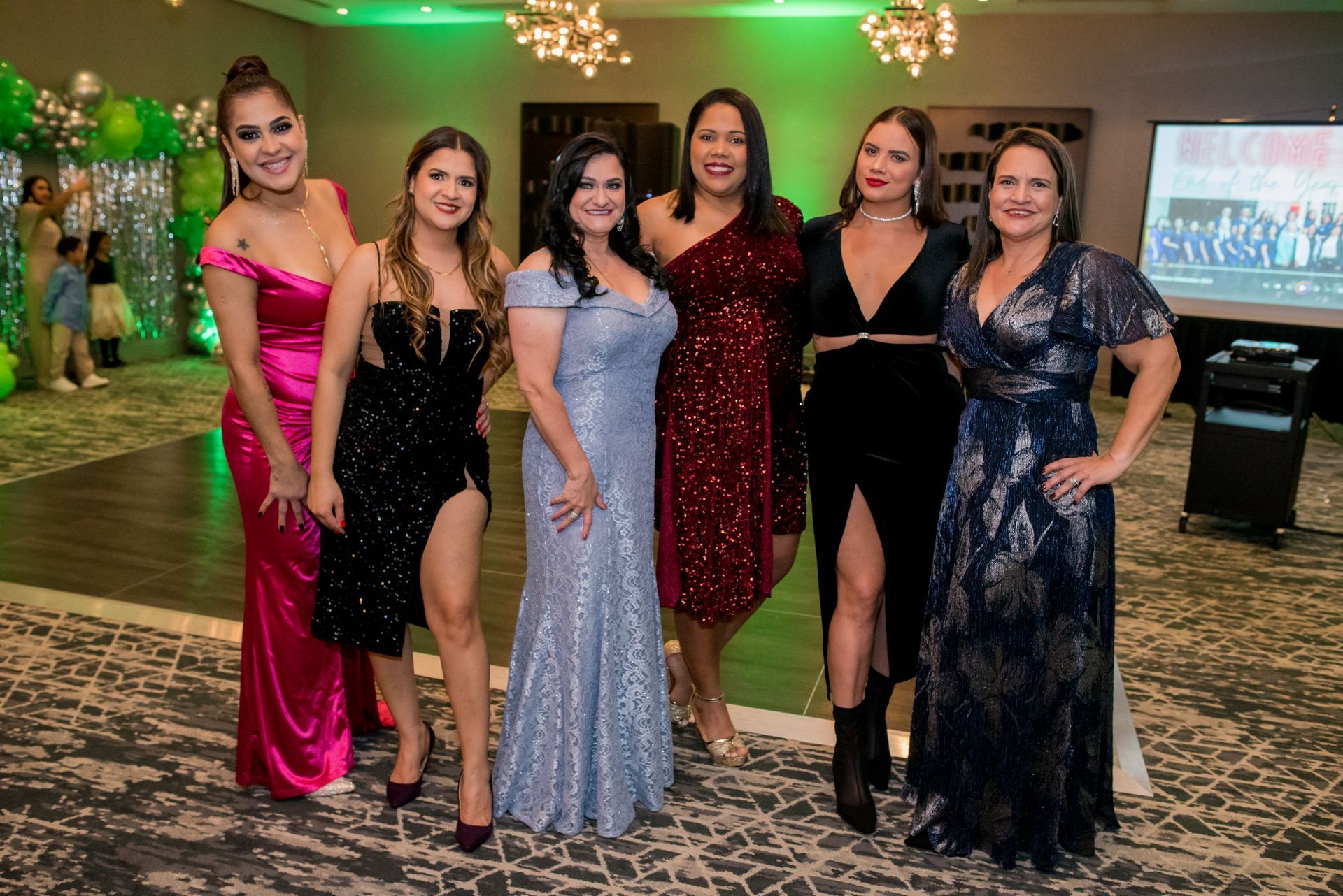 Group of six women in formal gowns, smiling at a celebratory event.