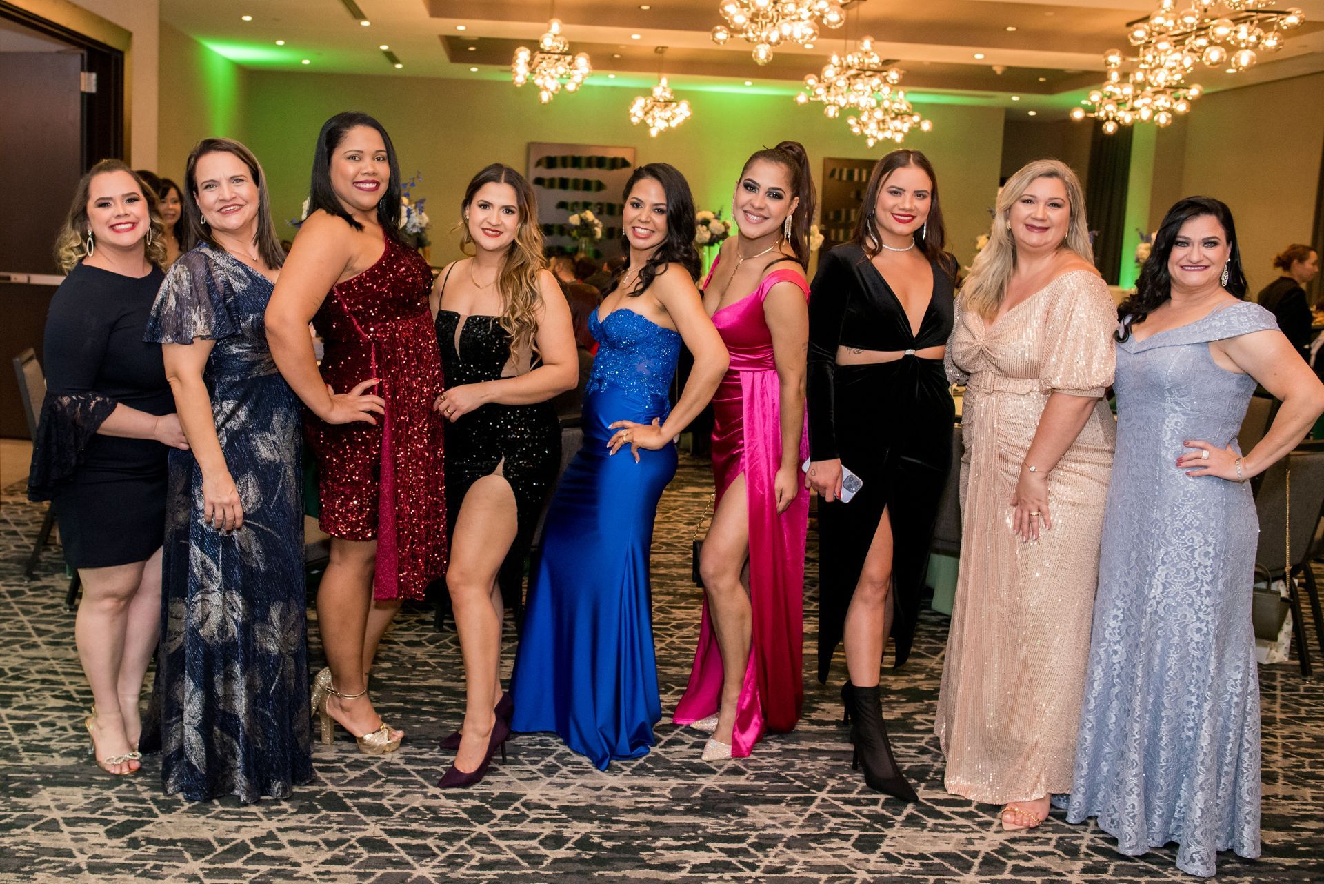 Group of elegantly dressed women posing together at a formal event, indoors.