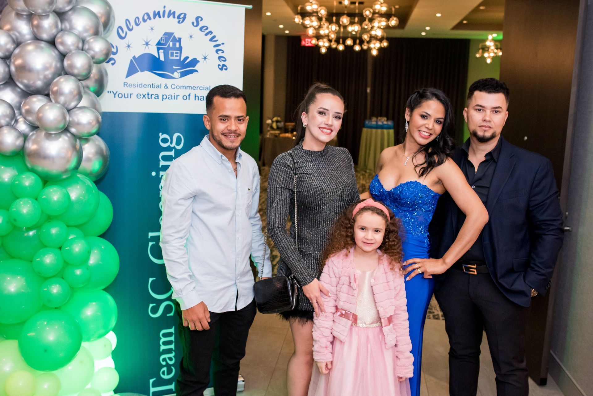 Group of people posing for a photo near a banner, with balloons, at an event.