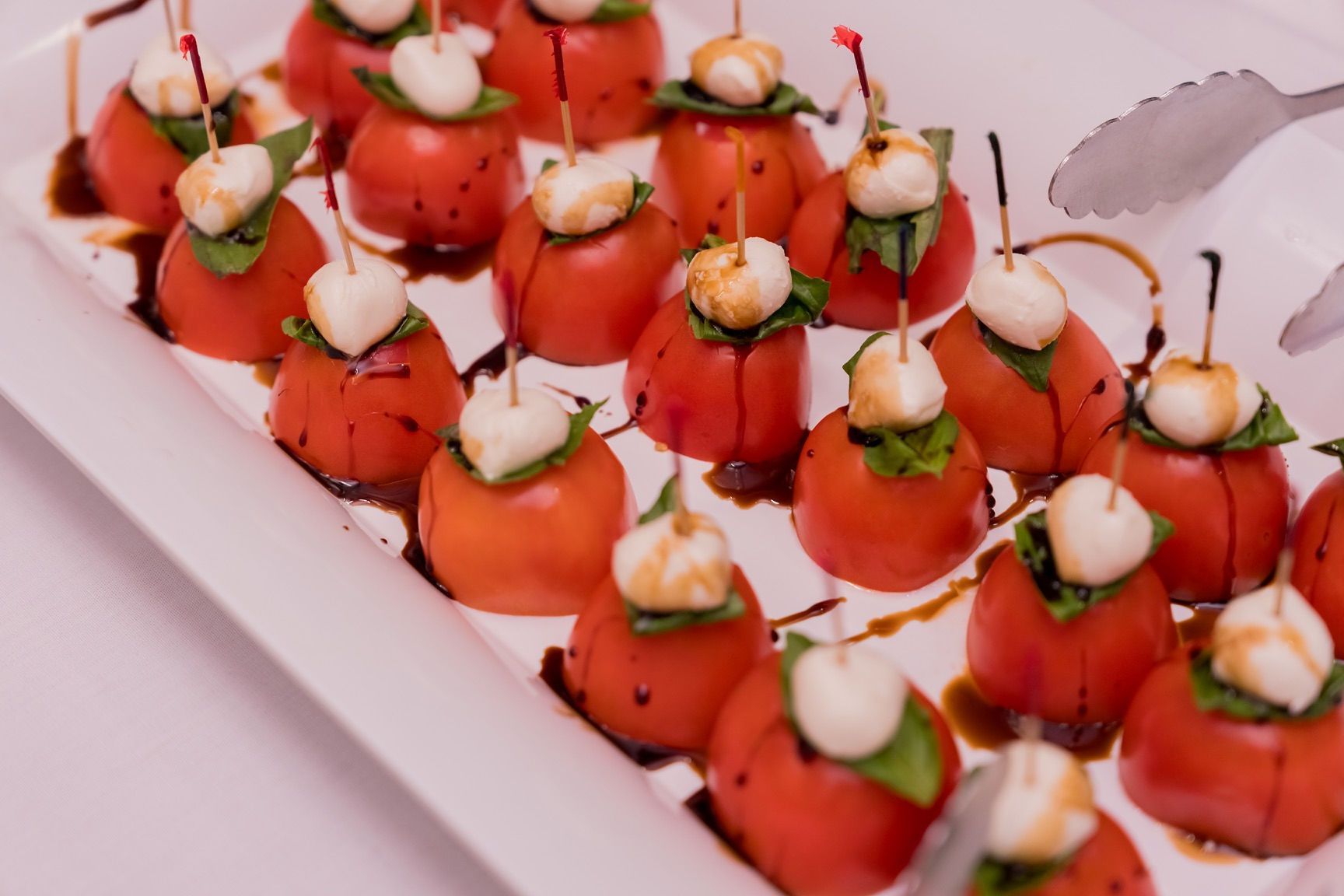 Caprese skewers: Tomatoes topped with mozzarella, basil, and balsamic glaze on a white platter.