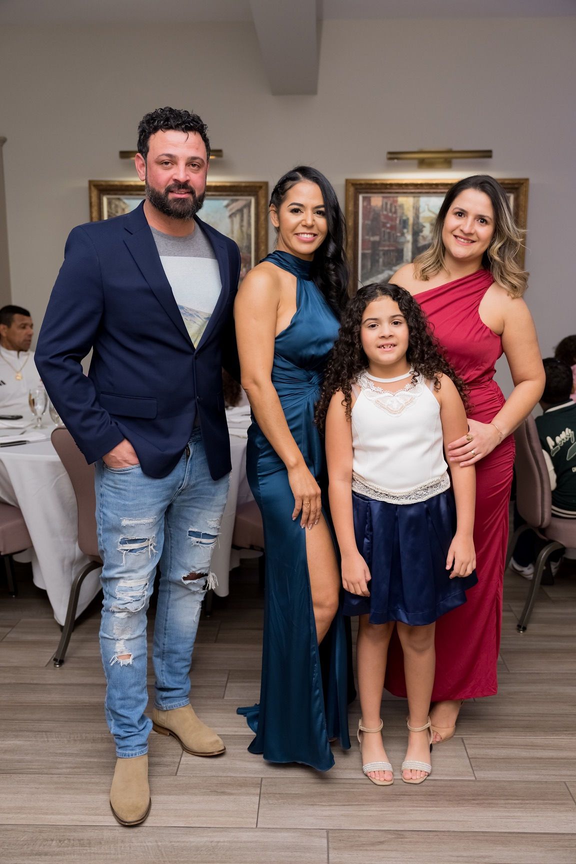 Family posing for a photo at an event. Man in blazer, woman in blue dress, girl in dress, woman in red.