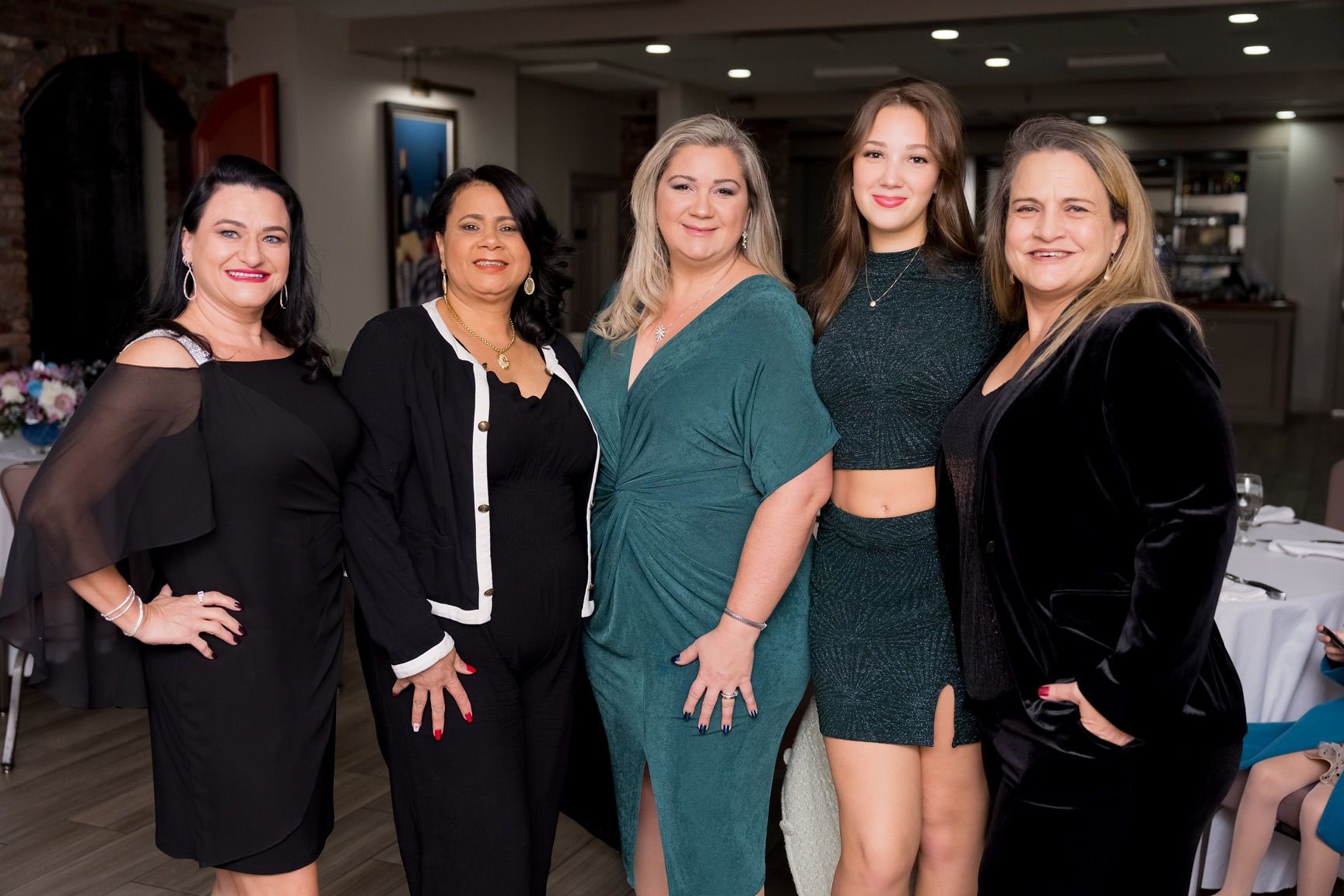 Five women pose together at an event, with elegant attire.