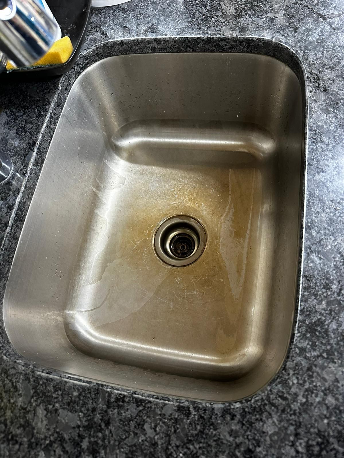 Stainless steel kitchen sink with brown stains.