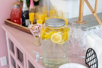 Pink-painted table with a water dispenser and lemon slices, drinks, and snacks for a party.