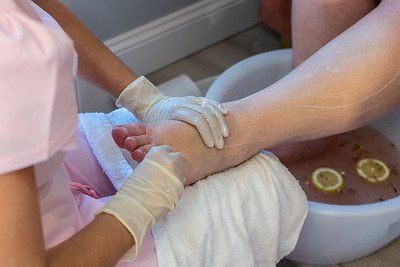 Person getting a foot massage. Hands in gloves rub foot above a basin of water with lemon slices.