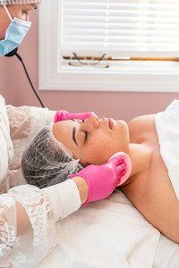 Facial treatment: Therapist with pink gloves cleanses a woman's face with pads in a spa setting.