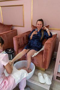 Woman enjoying pedicure, wearing a navy robe, pink spa chair, foot soak.