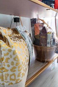 A gold and white patterned bag sits next to a wrapped gift basket on a wooden shelf.
