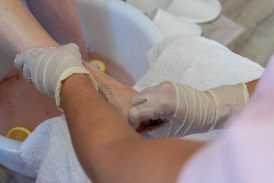 Person receiving foot treatment at a spa. Hands in gloves gently washing foot with a towel over a basin.